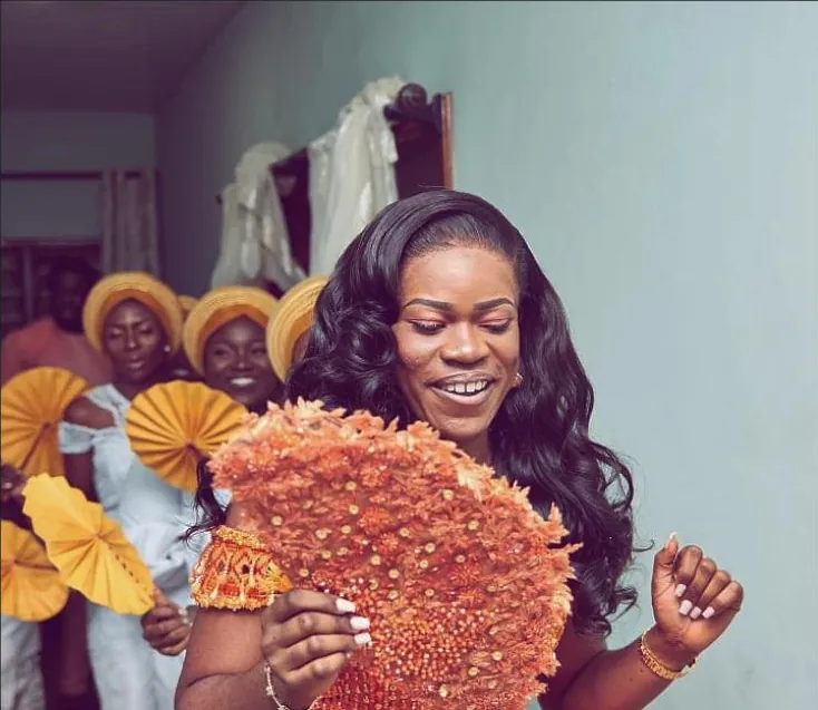 A bride holding a hand-beaded orange bridal fan, her bridesmaids standing behind her with matching gold fans.