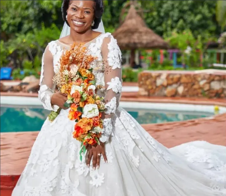 A bride in a white lace gown carrying a cascading bouquet of orange and cream flowers.